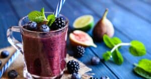 Verre de smoothie aux fruits rouges, figue et menthe, sur une table en bois.